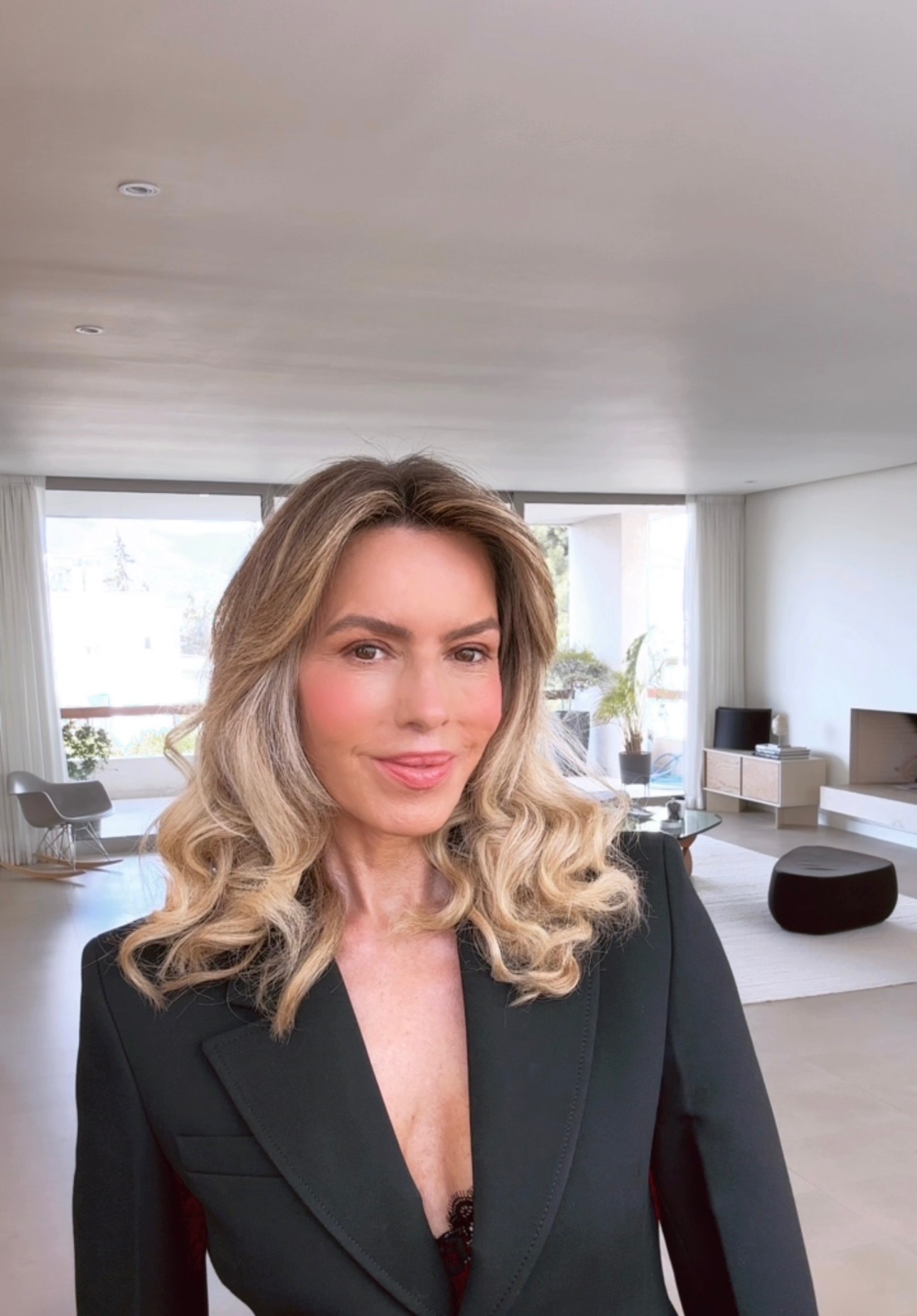 Esther Sarphatie smiling in a black blazer in a bright modern living room.